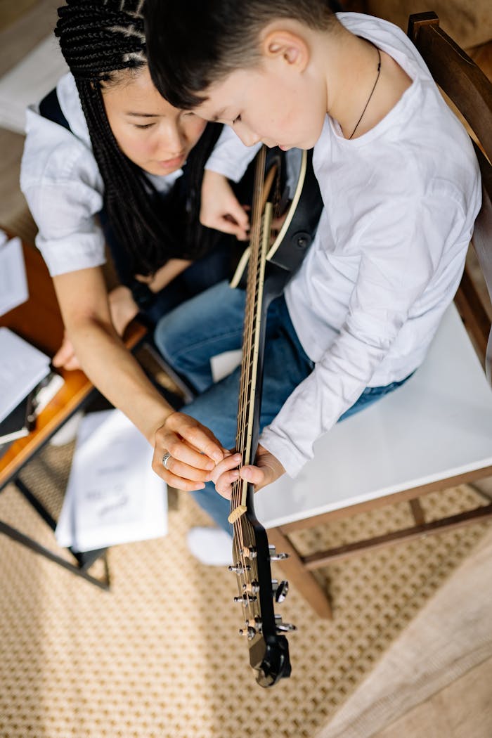 A woman teaches a young boy to play acoustic guitar indoors, fostering musical learning.